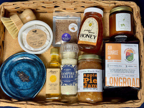 A Farmer’s Market Harvest Box filled with Jacksonville-made goods including honey, garlic salt, coffee, jam, olive oil, candle, dish soap, and a handmade blue spoon rest.